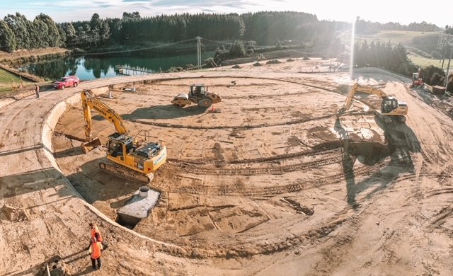 Excavators and a roller working inside a large pond excavation